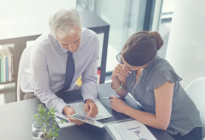 Senior male advisor and female colleague reviewing financial charts on a tablet.
